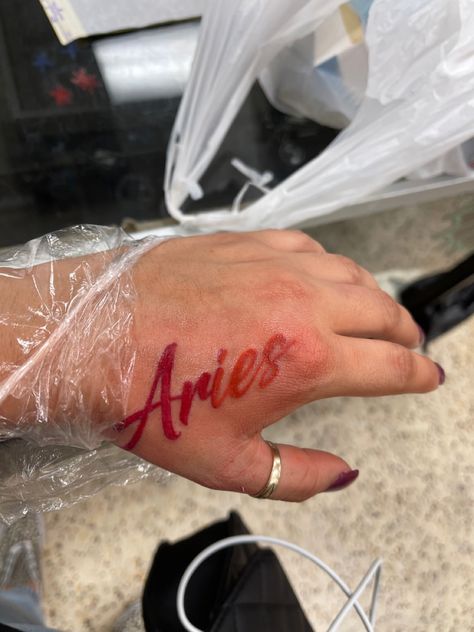 Red Ink Tattoo : Aries  
Hand placement Aries Tattoo Black Women, Aries Tattoo On Hand, W A Y S Tattoo Red, Cursive Red Ink Tattoo, Red Name Tattoo, Aries Red Tattoo, Aries Word Tattoo, Aries Neck Tattoo, Aries Hand Tattoo