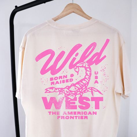 🤠Embrace the spirit of the Wild West with our "Wild West Born & Raised" graphic tee! This vintage-inspired shirt features a bold pink design that pays homage to the rugged American frontier. Perfect for your country concert or your night out in Nashville! 🔥 Stand Out in Style: Whether you're hitting the rodeo or just hanging out with friends, this graphic tee is sure to turn heads and start conversations. Pair it with your favorite jeans or shorts for a casual yet cool look that's perfect for any occasion.  🖤SHIRT MATERIAL Comfort Colors Unisex Shirt 100% Ring-Spun Cotton Printed using Direct To Garment style- Inks are printed directly into the fabric. Different sizing may effect placement of final design. Colors may differ slightly due to different user monitor and screen settings.  🏁 Country Concert Tshirts, Female Graphic Tees, Concert T Shirt Design, Trendy Oversized T Shirts, Fun Shirt Designs, Wild West Design, Punk Tshirt Design, Tour Tshirt Design, Club Shirt Designs