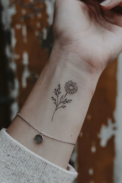 Flower tattoo on a wrist with a silver bracelet. Daisy Finger Tattoo Simple, Small Simple Nature Tattoos, First Tattoo Ideas Female, Flower On Hand Tattoo, Cross Floral Tattoo, Wrist Flower Tattoos For Women, Small Nature Tattoos For Women, Tiny Wrist Tattoos For Women, Minimalist Nature Tattoos