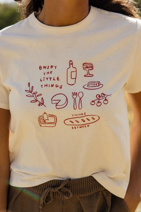 The cutest graphic tee is here! Featuring a little picnic on your shirt, the Enjoy The Little Things Tee is a cute take on a classic graphic. slightly sheer // paired with the come together tapered pants in darkolivegreen Simplistic Shirt Design, Popular T Shirts Graphic Tees, Tshirt Print Aesthetic, T Shirts Trendy, Garden T Shirt Design, Positive Quotes Tshirt, Fun T Shirt Ideas, 90s Graphic Tee Outfit, Flowers Tshirt Design