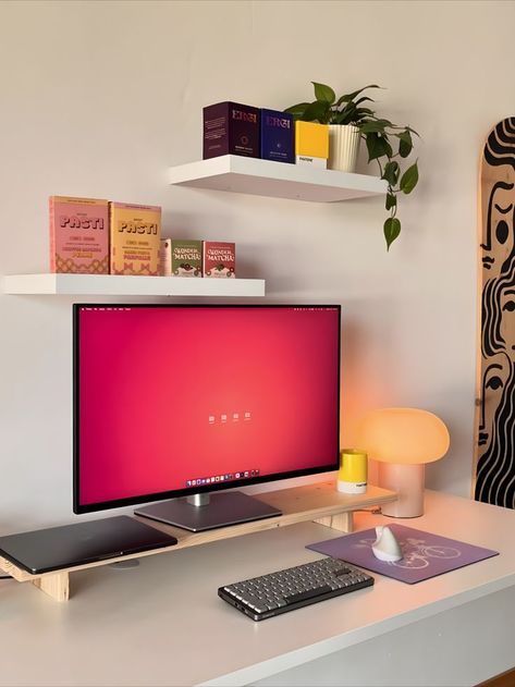 A minimalist and cozy home office setup featuring a large monitor on a sleek desk, surrounded by vibrantly colored decor items including books, a plant, and an artistic skateboard on the wall. The workspace is characterized by its clean design and pops of color that create a lively and inspiring environment. Townhome Decorating, Cozy Setup, Lighting Hacks, Indian Room, Lighting Tips, Cozy Home Office, Desk Inspiration, Aesthetic Space, Warm Lighting