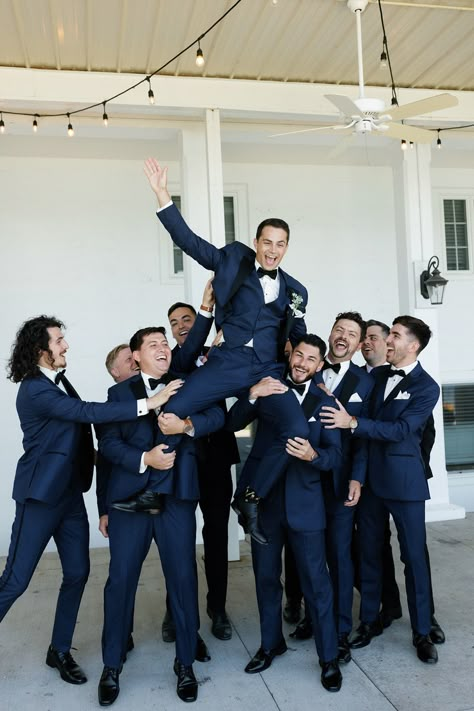 The couple wanted the wedding party to complement the environment of the venue in a timeless and upscale way that reflected the blue lake and beautiful surrounding greenery. The bridesmaids wore dusty blue Azazie dresses with soft, natural glam by LJ Artistry and Reborn Hair Company, and carried bouquets full of soft green, soft pinks, and creams. The groomsmen wore navy blue suits with black lapels and bowties from Men's Wearhouse. #lakewedding #groomsmen Groomsmen Attire Navy And Grey, Cobalt Blue Groomsmen Attire, Blue Tuxes Wedding, Navy Black Tie Wedding, Dark Blue Summer Wedding, Blue Tuxedo Wedding Groomsmen, Dark Navy Blue Groom Suit, Navy And Dusty Blue Groomsmen, Navy Blue Bridesmaids And Groomsmen