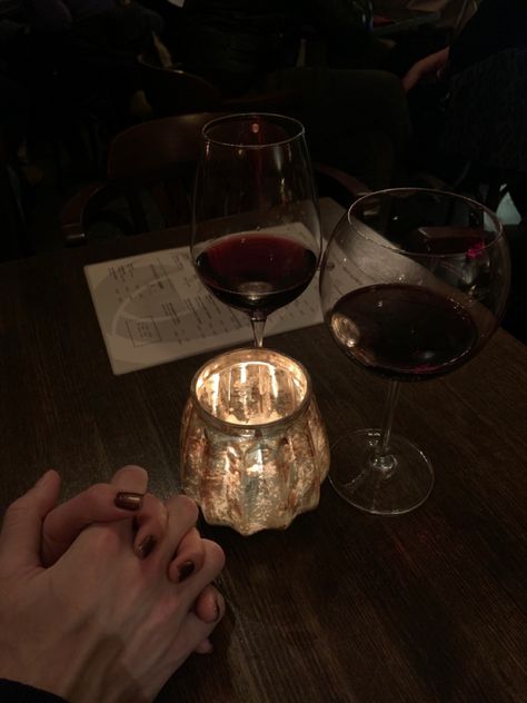 A couple holding hands under candlelight with two red wines Couple With Wine Photography, Red Wine Couple Aesthetic, Couple Drinking Wine Aesthetic, Red Wine Aesthetic Vintage, Couples Drinking Wine, Wine Club Aesthetic, Couple Drinking Wine Romantic, Aesthetic Paris Vintage, Maroon Taylor Swift Aesthetic