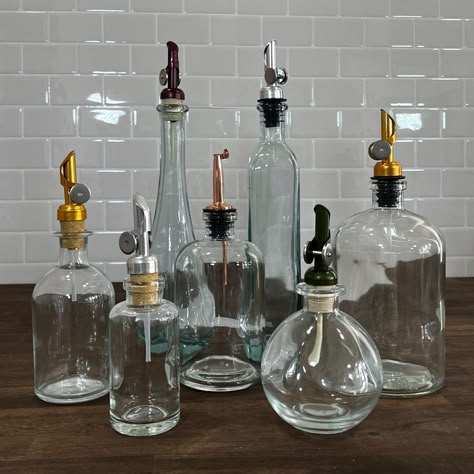 "Keep your kitchen organized and stylish with our glass apothecary style bottles.  Choose from a variety of shapes, sizes and colors.  Perfect for a gift or to keep for yourself!  The bottle arrives empty and ready to fill! DETAILS: *Multiple sizes, colors and shapes *Multiple pour spout options to choose from with either a cork or rubber base *BPA and Lead Free *Removable weighted pour spouts keep the contents contaminant free *Easy to remove for quick filling and easy hand washing MEASUREMENTS: *4oz Bottle:  2\"w x 4.25\"h *8oz Bottle (All Colors):  2.5\"w x 5.75\" h *8.5oz Moon Bottle:  3.5\"w x 4\" h *11.8oz Teardrop Bottle (All Colors): 3.25\"w x 9.75\" h *12.5oz Rectangular Bottle:  2.25\" w x 9.75\" h *16oz Bottle (All Colors):  3.25\"w x 6.5\" h *25oz Bottle: 4\"w x 7.25\" h *Spout Oil Bottles Kitchen Storage, Glass Oil Bottles, Apothecary Kitchen Decor, Apothecary Aesthetic Kitchen, 1800s Apothecary, Vintage Bottles Decor, Apothecary Kitchen, Oil And Vinegar Bottles, Apothecary Design