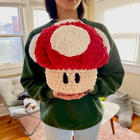 The only thing cuter than a mushroom crochet plushie is a MARIO MUSHROOM PLUSHIE! This soft, huggable plushie (which doubles as a decorative crochet pillow) is a super fun project for crochet beginners. It's irresistibly cute and brings back memories of my childhood spent playing Mario Kart on the Wii. Plus, it's the perfect gift for anyone who loves video games or quirky home decor! This 8-page mushroom crochet pattern includes an in-depth breakdown of the steps needed to create your own easy crochet plushie. It features photos of the most important steps along the way and additional notes to help beginners fully understand the pattern. No prior crochet experience is necessary, though you'll want to practice some basic stitches (single crochet and half double crochet) for a few minutes be Crochet Pillow Mushroom, Mario Crochet Ideas, Mario Mushroom Crochet Pattern, Mushroom Crochet Pillow, Large Crochet Mushroom, Free Chunky Crochet Patterns, Crochet Mario Characters, Mario Crochet Pattern Free, Crochet Mario Mushroom