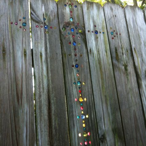 I had seen the random marble placement of marbles in a fence and decided to create a cross. My awesome husband went to craft store with me where we found no marbles and decided to go with glass beads. We cut a couple of bead strands that were made for necklaces and bought a box of mixed beads. Awesome husband continued awesomeness by drilling all the holes for me after we drew a cross with a level for only a simple outline. The rest was freehand.  Try it! It's fun and when the light gets behind Marble In Fence, Marbles In Fence Holes, Fence With Marbles In It, Marbled Fence, Marbles In Fence, Marble Fence, Awesome Husband, Pallet Fence, Timber Fencing