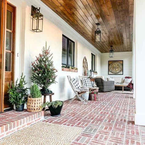 A classic basket weave pattern is used to install a warm, rustic red brick porch with a roof extension. The white exterior siding contrasts with the brick and the warm wood paneling along the ceiling. Modern farmhouse black lanterns hung from the ceiling complete the farmhouse look. White House With Red Brick, Red Brick Porch, White Brick House Exterior, Brick Patio Ideas, House With Front Porch, Modern Farmhouse Black, Brick Porch, Patio Fan, White Porch