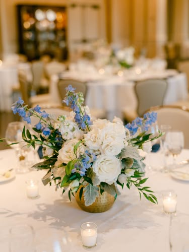 A simple, sweet floral arrangement for this DC wedding! You can never go wrong with florals for your table centerpieces, especially with candles. This arrangement is filled with cream wedding flowers, greenery textures, and pops of blue wedding flowers. #DCBrides #DCWeddings #DCWeddingFlorist #WeddingFlowers Wedding Table Decor Dusty Blue, Round Table Centerpieces Wedding Simple, Wedding Table Simple, Table Flower Centerpieces, Round Table Centerpieces Wedding, Floral Table Centerpieces, Outdoor Engagement Party, Round Table Centerpieces, Cream Wedding Flowers