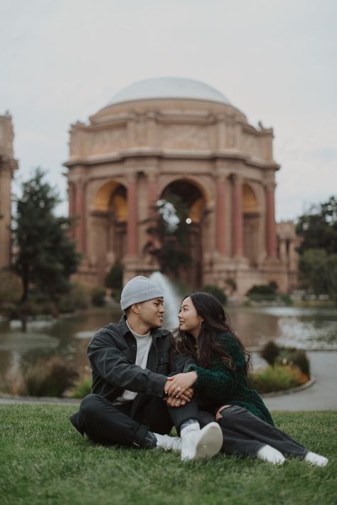 a man in a grey beanie sitting in the grass next to a brunette woman in a green fuzzy cardigan looking at each other and smiling with the dome and fountain of the palace of fine arts in san francisco in the background Golden Gate Park Photoshoot, Palace Of Fine Arts San Francisco Engagement, Golden Gate Bridge Picture Ideas Couples, San Francisco Couple Pictures, Palace Of Fine Arts Photoshoot, Palace Of Fine Arts Engagement Photos, Golden Gate Park Engagement Photos, Pink And Blue Sunset, San Francisco Engagement Photos