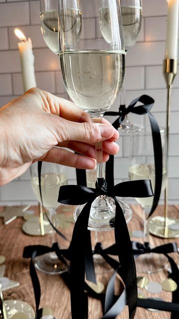 •Stephanie Bryant• on Instagram: "the bow trend?! I’m obsessed! 😍 the perfect finishing touch to a New Year’s Eve (or anytime) party 🎀🥂🥂 here is how I make mine Tie a knot onto your glass then form two bunny ears - cross the right one over the left then loop behind and thread it back through the center - pull both ears to tighten then pull on the ends until you’ve reached your desired size and shape bow! Make sure to save this reel and follow @the_blonde_kitchen for more entertaining tips! 🖤🤍 #theblondekitchen #tbksocialclub #supperclub #newyearseve #bowtrend #bow #partyideas #entertainingathome #tablesetting #tablescapes #entertainingideas #newyears #champagne #fayettevillear #holidayinspo #decorideas #partyinspo" New Years Eve Bachelorette Party, We’re Tying The Knot Engagement Party, New Years Eve Wedding Ideas Decorations, Engagement Party New Years Eve, Tie The Knot Engagement Party, Bow Champagne Glasses, Timeless Bachelorette Party, Champagne Glass With Bow, Glasses With Bows