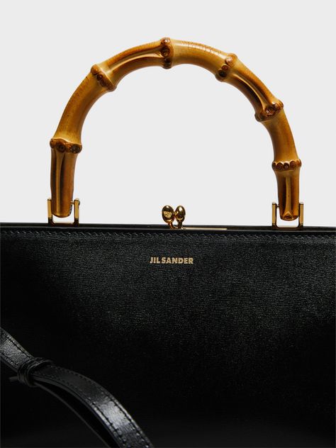 Jil Sander's Goji Small Bamboo Bag in Black features a metal frame and embossed Jil Sander logo. This rectangular leather shoulder bag comes with a detachable and adjustable strap and bamboo top handle. Made from 100% calf leather with a nappa lining and inner zipped pocket.