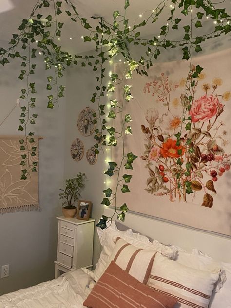 fairy garden themed bedroom with hanging vines, fairy lights, and floral decor Vines In Bedroom Slanted Ceiling, Pink Room With Vines, Bedroom Inspirations Vines, Vines In Shower Decor, Vines On Slanted Ceiling, Vine Ceiling Bedroom, Vines On Roof Bedroom, Ivy Vines Bedroom, Vines In Bedroom Ceiling