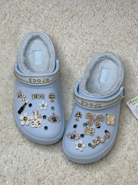 Cream coloured carpet with light blue crocs with gold charms and chains White Crocs Jibbitz Aesthetic, White Crocs With Gold Charms, Black Crocs With Gold Jibbitz, Light Blue Crocs With Charms, White Croc Jibbitz Ideas, Light Blue Crocs Outfit, Blue Crocs Aesthetic, Mineral Blue Crocs, Blue Crocs With Charms