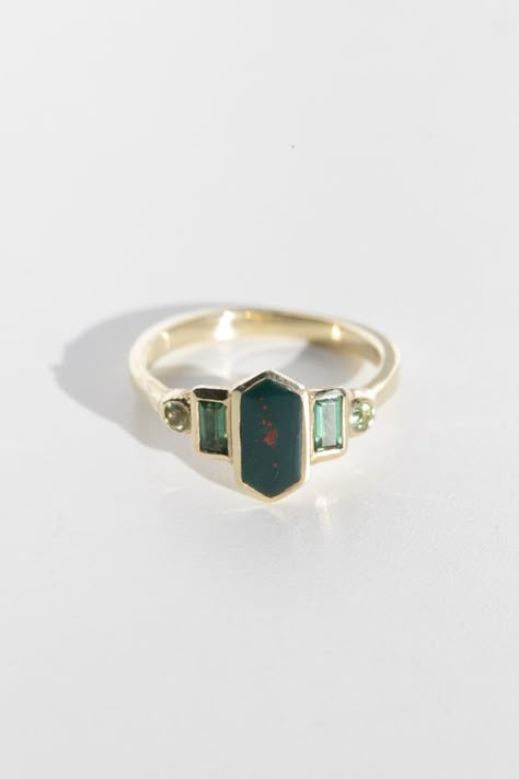 Art deco inspired ring with bloodstone and green tourmaline.

Bloodstone is inlaid into the elongated hexagon, measuring 9.5mm x 5mm. Accent tourmalines are approximately .30 total carat worth. Millimeter measurement from end to end is 15mm. Horizontal Gemstone Ring, Art Deco Ring Emerald, Artist Engagement Rings, Bloodstone Ring Engagement, Emerald Green Engagement Rings, 5 Stone Engagement Rings, Bloodstone Engagement Ring, Green Garnet Ring, Baguette Band Engagement Ring