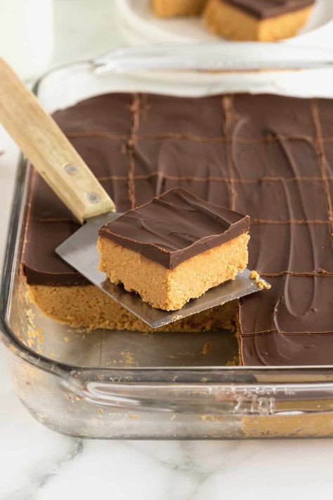 A no-bake chocolate peanut butter bar on a metal spatula with a wooden handle in front of a baking dish of chocolate peanut butter bars. Peanut Butter Dessert Bars, Buckeye Bars Recipe, Chocolate Peanut Butter Squares, Chocolate Dessert Bar, Butter Squares, Peanut Butter Bar, Peanut Butter Oat Bars, Easy Christmas Cookies, Chocolate Peanut Butter Bars