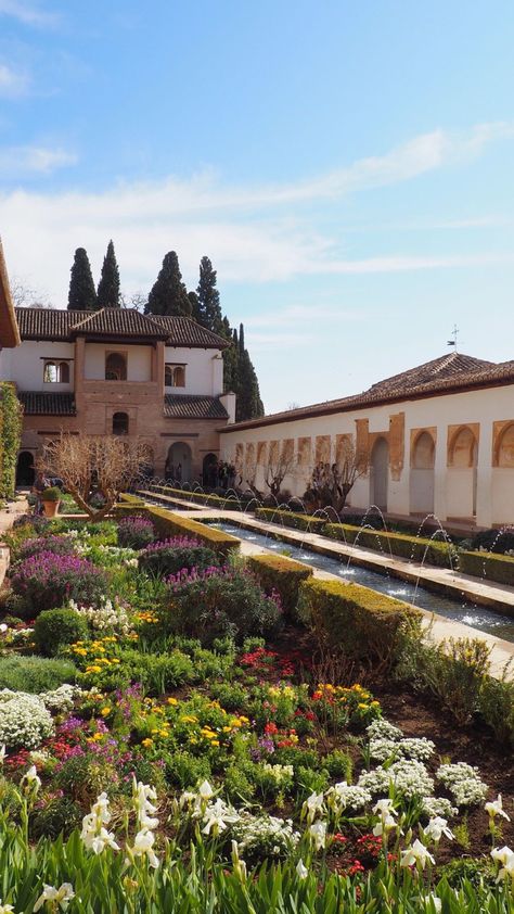 A photo of the flower garden at the Alhambra palace in Granada, Spain. The skies are blue and the flowers are multiple colors that line a fountain down the middle of the garden. Granada Alhambra Palaces, Granada Spain Aesthetic, Alhambra Garden, Islamic Gardens, Spanish Palace, Spanish Landscape, Andalusia Travel, Alhambra Spain, Spring Gardens