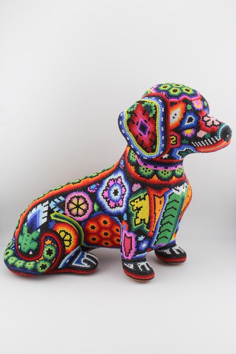 Celebrate the vibrant heritage of Huichol art with these remarkable beaded dachshund sculptures. Handcrafted from natural clay and intricately decorated with thousands of tiny Huichol beads, each sculpture showcases the artistry and spiritual significance of one of Mexico's oldest indigenous art forms. Each bead is meticulously placed using agave needles, creating captivating geometric designs that hold deep cultural meaning. The patterns depicted are symbolic representations of the Huichol people's connection to nature, spirituality, and the universe. These vibrant dog sculptures are not only a tribute to the Huichol culture but also a unique piece of decor that brings color and cultural history to your home. Perfect as a statement piece or gift, they represent both the artisan's skill an Huichol Beading Pattern, Beaded Dachshund, Nature Spirituality, Latin Art, Blue Dachshund, Huichol Art, Symbolic Representation, Monterey Ca, Punch Needle Patterns