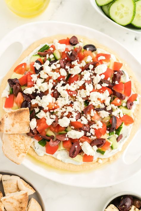 If you want a filling snack that keeps you satisfied, you will love this Hummus Dip. It is a Greek-style recipe that is made with hummus, tzatziki, cucumbers, tomatoes, olives, and feta cheese. Layered Hummus Dip, Layered Hummus, Greek Appetizer, Mediterranean Snacks, Greek Dip, Greek Appetizers, Baklava Recipe, Wheat Thins, Homemade Tzatziki