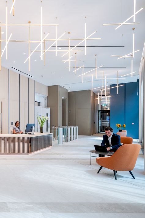 office interior design with large suspended lighting in a reception area Reception Ceiling, Office Reception Design, Office Reception Area, Office Ceiling, Acoustic Ceiling, Office Reception, Suspended Lighting, Reception Design, Reception Area