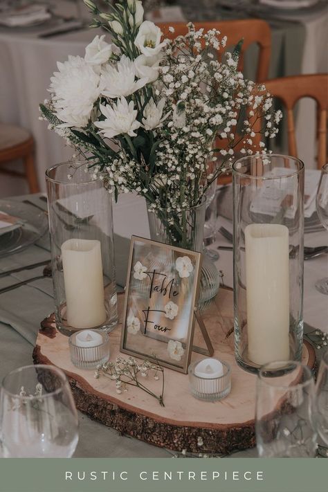 log slice, candles, green and white flowers, table number as a wedding centrepiece Wedding Decor Wood Slices, White Rustic Wedding Theme, Centerpieces Wedding With Table Numbers, Natural Wedding Centre Pieces, Sage Green Wedding Centre Pieces, Wedding Wooden Centerpieces, Wedding Top Table Flowers Rustic, Green Table Centrepiece, Log Slice Centrepiece