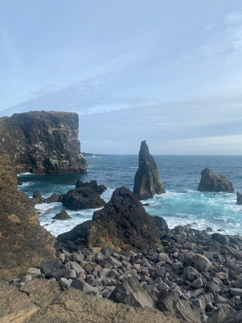 A photo of an Icelandic shore with rocks in the foreground which open up to blue waters. A cliff can be seen in the background on the left. Rocky Shore Aesthetic, Sea Cliff Aesthetic, House On A Cliff By The Sea, Iceland Summer, Ocean Cliff Aesthetic, Rocky Sea Shore, Dream House Aesthetic, Rocky Ocean Shore, Ocean Shores