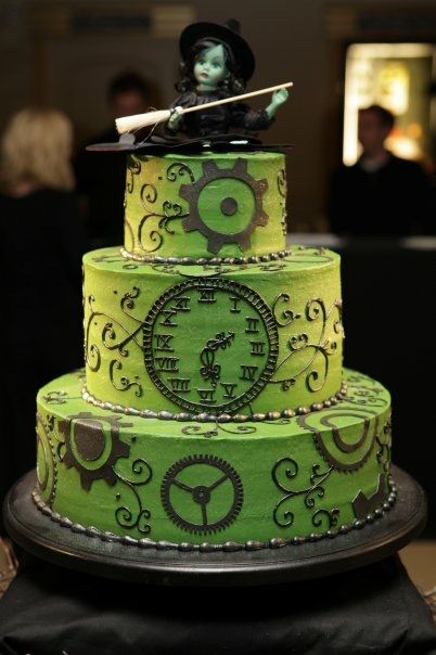 the Wicked cake was decorated with clock parts and gears replicating the sides of the stage at the Gershwin Theatre on Broadway in New York and topped with a Madame Alexander Elphaba doll. #wicked #broadway #birthdaycake (Ashley Bakery, Charleston, SC) Broadway Sweet 16, Clock Cake, Theatre Cake, Wicked Party, Shaped Eyebrows, Halloween Wedding Cakes, Fantasy Cake, Wicked Witch Of The West, Witch Of The West