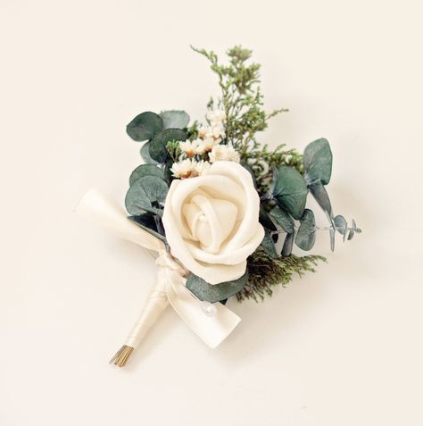 "This dried flower and greenery boutonniere creates a sweet and simple boho-inspired look. It features sprigs of dried greenery, small ivory star flowers, eucalyptus, and a center of ivory sola wood flower.  NOTE - some people do not like the natural scent of the caspia! please be aware that is does have a strong scent.  DETAILS  ♥ Listing is for one boutonniere - including pin.  ♥ Each measures about 3.5\" tall. -- WG" Groomsmen Buttonaire, Boho Boutineer Ideas, Bouteneire Groomsmen, Dark Green Boutonniere, Mother Of The Bride Corsage Pin, Green Corsage And Boutonniere, Wood Flower Corsage, Eucalyptus Corsage, Greenery Boutonniere