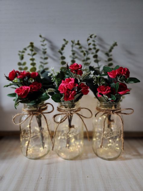 "These beautiful faux mini-rose quart size mason jar centerpieces are a Glassy Gal original design. Each centerpiece includes one set of warm white LED fairy lights, a jute bow, a deluxe faux greenery arrangement with mini roses. You can choose your mini rose color at checkout. These centerpieces are very popular for weddings, baby showers, parties, corporate events, holiday events, and any other event that requires table centerpieces. They also look great in any room of your house or office. To see other lighted jar options and all of my other listings, please view my shop: https://www.etsy.com/shop/GlassyGalDecor Each jar set includes: (1) clear quart size mason jar (1) set of LED fairy lights (1) deluxe faux greenery arrangement (includes 3 tall eucalyptus stems, 2 short silver dollar Table Decoration With Lights, Restaurant Centerpieces Simple, Small Elegant Centerpieces, Red And Gold Centerpieces Wedding, Rose Themed Birthday Party Decorations, Simple Rose Centerpiece, Black And Red Centerpieces, Valentine Table Centerpieces, Red And Gold Centerpieces