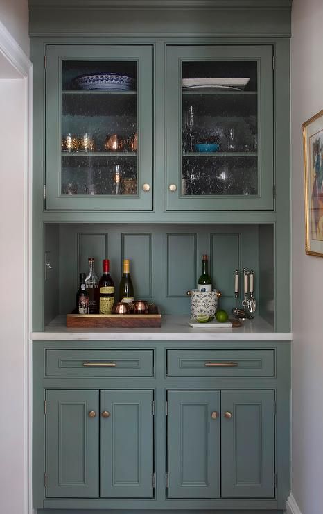 Fitted in a kitchen nook, hunter green bar cabinets accented with brass hardware are topped with a honed marble countertop fixed against a hunter green wood-paneled backsplash and beneath glass front cabinets. Sage Green Bar Cabinet, Benjamin Moore Garden Oasis, Dark Green Coffee Bar, Garden Oasis Benjamin Moore, Sage Forest, Erin Gates Design, Bar Nook, Brass Mesh, Sage Green Paint