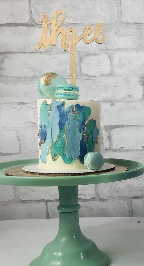 A stunning 3rd birthday cake with a white buttercream base, swipes of blues and teals, aqua macarons, and a gold "three" topper! Aqua Cake Ideas, Turquoise And Gold Birthday Cake, Aqua Birthday Cake, Blue And Green Cake Birthday, Teal Birthday Cake For Women, Teal Cakes, Teal And Gold Cake, Blue And Green Cake, Teal Birthday Party Ideas