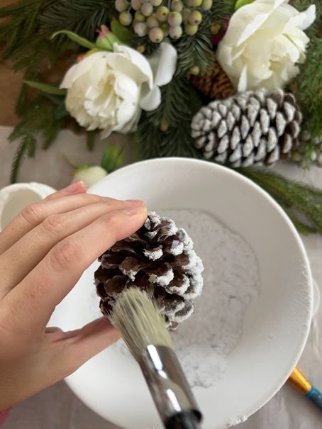 This DIY project will add a touch of winter magic to your home! Using flocking powder, turn plain pinecones into frosted, snowy beauties that are perfect for winter decorating. Follow our step-by-step tutorial and have a basket full of frosted pinecones in no time. These DIY pinecones will bring a touch of winter wonder to any room. Grab your flocking powder and pinecones, and let's get crafting! Diy Frosted Pinecones, Prepping Pinecones For Crafts, Pinecone Winter Crafts, Spray Painting Pine Cones Diy, Bleached Pinecones Diy, Decorate Pinecones For Christmas, Christmas Pinecone Wreaths Diy, Pinecone Garland Diy How To Make, Snow Covered Pinecones