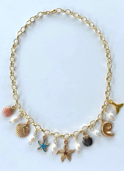 Dive into summer with our Coastal Seashell Charm Necklace! Unveil your summer glow with the perfect charm gold charm necklace. A dazzling tribute to the beauty of the ocean and the magic of sunny days.  At the heart of this enchanting piece is a radiant gold starfish, embodying the spirit of the sea and the elegance of gold. A stunning focal point that captures the sea's spirit. Surrounding it are vibrant seashells in a shimmering pink and dramatic black for a playful burst of color. Smaller colorful starfish charms add a touch of sparkle and whimsy. Luminous pearls add a chic contrast, enhancing the necklace with timeless elegance. Whether going to summer parties, casual dinners with friends, or attending special events, elevate your look effortlessly with the perfect coastal charm neckla Gold Summer Jewelry, Seashell Charm Necklace, Beach Charm Necklace, Shell Charm Necklace, Surf Jewelry, Travel Necklace, Preppy Jewelry, Pretty Jewelry Necklaces, Jewelry Accessories Ideas