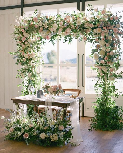 A dreamy pastel wedding arch covered in florals for a wedding sweetheart table. 🌸 Click through to rent an arch for your Utah wedding.   @haileyhbonny @heathernan @riverbottomsranch   #weddingarch #floralarch #weddingarchinspo #weddingdecor #weddingsweethearttable #sweethearttableinspo #weddingdetails #weddingflorals #pastelweddingflowers #pastelbouquet #pastelwildflowers #wildflowerwedding #summerwedding #springwedding #springweddingdecor Sweetheart Table Installation, Sweetheart Table Wedding Arch, Sweetheart Table Wildflowers, Arch Behind Sweetheart Table, Pastel Wedding Arch, Pastel Floral Decor, Sweatheart Table, Styling Moodboard, Sweetheart Table Backdrop