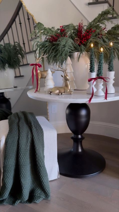 A gold or red vase with fresh poinsettias, holly sprigs, or a scented candle wrapped in greenery. Black Bench Front Porch, Entry Way Table Christmas Decor, Christmas Foyer Decor, Holiday Entryway Decor, Nutcrackers Display, Round Entry Table, Christmas Dining Table Decorations, Holiday Entryway, Christmas Foyer