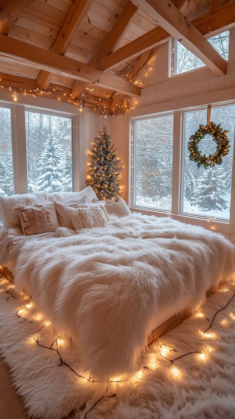 Cozy bedroom with white fur blankets, twinkling Christmas lights, a wreath, and snow-covered trees visible through large windows. Cozy Winter Aesthetic Christmas, Christmas Decorating Aesthetic, Christmas Magic Aesthetic, Cozy Christmas Decor Bedroom, Christmas Decor Ideas For Small Spaces, Cozy Holiday Aesthetic, Room Ideas Calm, Aesthetic Christmas Room Decor, Christmas Tree In Bedroom