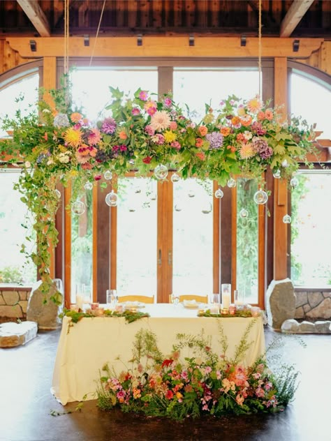 Bright Hanging Floral Installation, Wild Flower Floor Arrangement, Flower Installation Hanging, Wildflower Hanging Installation, Freeform Flower Arrangements, Wildflower Bride And Groom Table, Wildflower Top Table, Hanging Flowers Above Table, Wild Flower Sweetheart Table