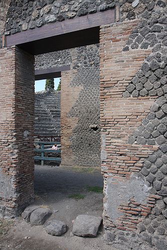 Brick Quoining: Pompeii Odeon - "A view of a doorway behind the stage building of the Odeon (music hall) of Pompeii. Concrete walls are faced with lava stones. Door jambs have been quoined with fired brick to create sharp corners. The lintel over the door is a modern replacement. * The general diagonal placement of the lava (dark gray) facing stones leads J.-P. Adam to classify this wall construction as opus quasi reticulatum (Adam 1974, 131). Date: ca. 80 B.C." Stone Lintel, Roman Garden, Pompeii Italy, Wall Brick, Masonry Work, Tree Growing, Pompeii And Herculaneum, Concrete Walls, Empire Romain