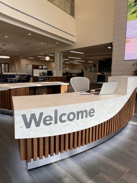 First Premier Bank in Sioux Falls recently opened the doors to their new main branch on 14th & Minnesota Avenue.  We are excited to share with you the custom bank millwork project we built and installed for them.  The project involved the main lobby reception desk/credenza, the refreshment center, kids corner, teller line and back wall including logo, coffee bars on all 5 floors, Express Banking area, and media wall. #bankreceptiondesk #cambriacountertops #coffeebar #conferenceroomtables Custom Reception Desk Design, Half Circle Reception Desk, Library Reception Desk, Luxury Office Building, Reception Seating Area, Round Reception Desks, Bank Lobby, Desk Credenza, Lobby Reception Desk