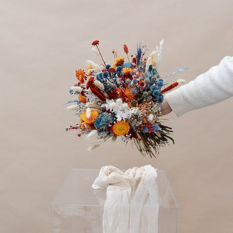 This beautiful bouquet includes a stunning combination of burnt orange and blue dried flowers, perfect for your wedding day. Our Colourful Dried Flowers Bridal Bouquet will make your special day even more special! Colourful Dried Flower Bouquet, Blue And Orange Fall Flower Arrangements, Dried Floral Bridal Bouquet, Cornflower Blue Fall Wedding, Small Colorful Wedding Bouquet, Blue Orange Bouquet, July Wedding Bouquet, Blue And Orange Bouquet, Orange And Blue Bouquet