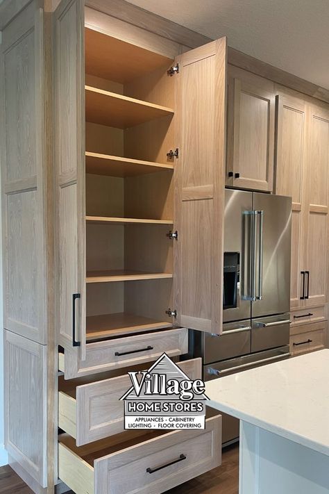 image of light white oak kitchen design with doors and drawers open on tall pantry cabinet. Black and white Village Home Stores logo in lower third of pin image. Built Pantry Cabinet, 30 Inch Pantry Cabinet, Pantry Using Wall Cabinets, Kitchen Pantry With Drawers, Fridge Between Pantry Cabinets, Pantry Storage Drawers, Pantry By Refrigerator, Deep Pantry Drawers, Galley Kitchen With Pantry Cabinet