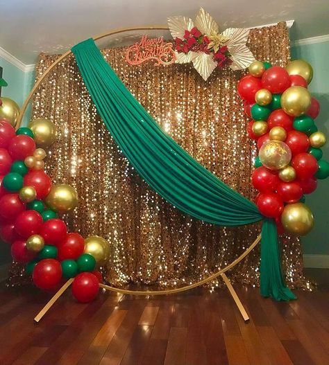 Set up a sparkling backdrop for your Christmas party using attractive decor elements. Cover the backdrop stand with shimmery gold sequin curtains for an enticing allure. Place a gold round arch at the front and arrange red, gold, and green balloons on it to impart a peppy appeal to your party decor. Also, stylishly drape green fabric and arrange red flowers along with gold leaves on the stand oozing oodles of glimmer and shimmer. Backdrop With Curtains, Flowers And Balloons, Sequin Curtains, Christmas Party Backdrop, Christmas Balloon Decorations, Birthday Decorations At Home, Deco Ballon, Luxury Christmas Tree, Work Holiday Party