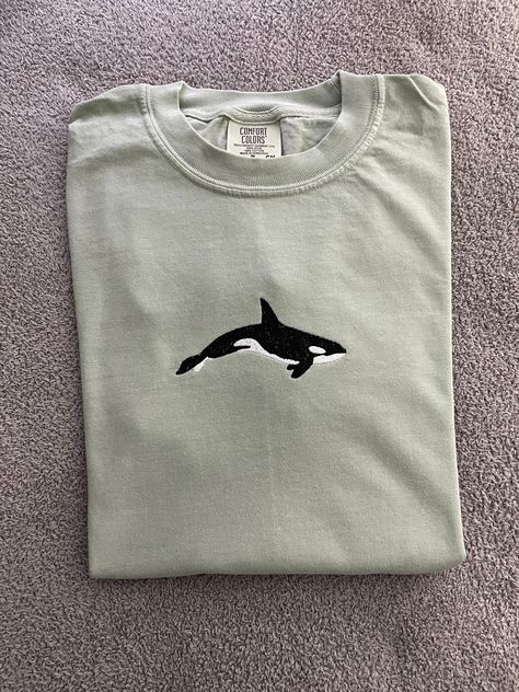 Orca embroidered on short sleeve t shirt Message me for sizes that are not listed!  Shirt:  Comfort Colors short sleeve Bay t shirt 6.1 oz., 100% ringspun cotton Care Instructions:  Machine wash cold, hang to dry  Material on the back of the embroidery is designed to stabilize the shirt as it is being embroidered, it will soften over time with more washes. Visit my Etsy for more animal-Inspired clothing : https://Stitchesbylindseyk.etsy.com Orca Embroidery, T Shirt Embroidery Ideas, Aztec Clothing, T Shirt Message, Embroidery Shirts, Groovy Clothes, Embroidered T Shirt, Ocean Shirt, Orca Whale