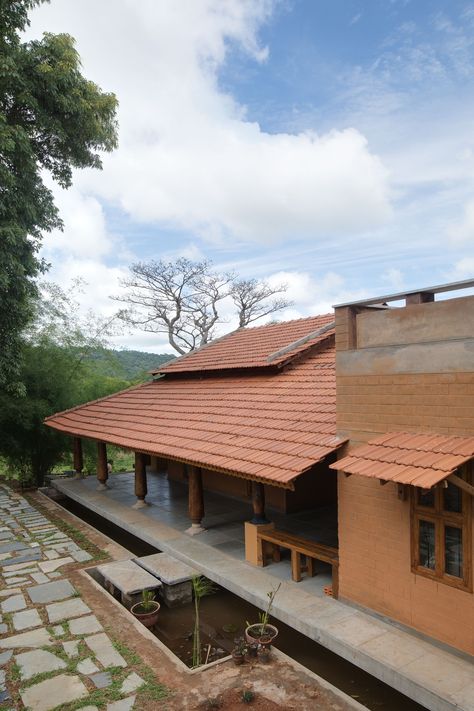 Ra Maram located in Manchi reserve forest has been designed to align with the principles of cradle to grave concept, minimising the carbon footprint and embodied energy of the construction. The walls are of stabilised mud blocks with the foundation and certain feature walls, being of local Sadarhalli stone, sourced and sized from within the site. The wood was re-purposed from an abandoned factory near-by. #CSEB #Mangalore tile roof #Earth architecture Mud House Exterior, Tiled Roof House, Mud Homes, Tiled House, Mud Houses, Mud Wall, Tile Roof, Roof Tiles Design, Roof Ideas Architecture Design