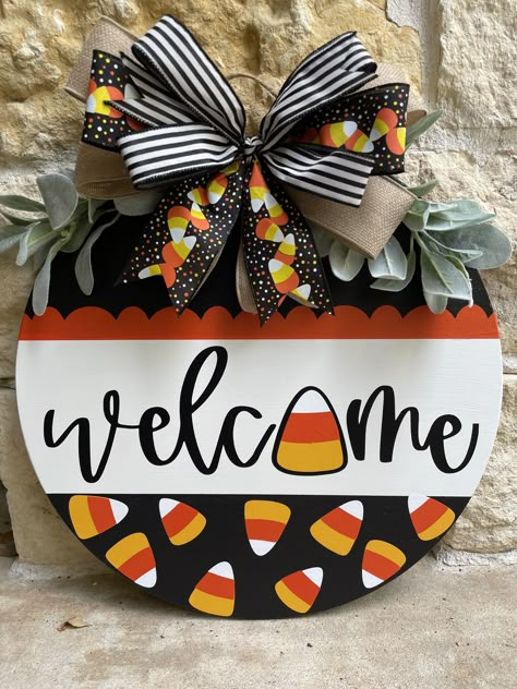 "What a great way to welcome friends and visitors to your home this fall! This candy corn Welcome door hanger is sure to show your Halloween spirit!  Door hanger has a stained base with black and white paint and candy corn vinyl design. Lambs ear and multi layered bow adorn the top.  If you would like the door hanger done in a different color combo, simply message us.  I cannot promise exact ribbons on bow.  Something comparable will be provided. Please allow 1-2 weeks processing time for your o Fall Halloween Door Hangers, Diy Fall Decorations For Home, Candy Corn Door Hanger, Diy Halloween Door Hanger, Fall Door Hangers Diy, Diy Fall Door Hangers, Halloween Wooden Signs, Halloween Door Signs, Round Door Hangers