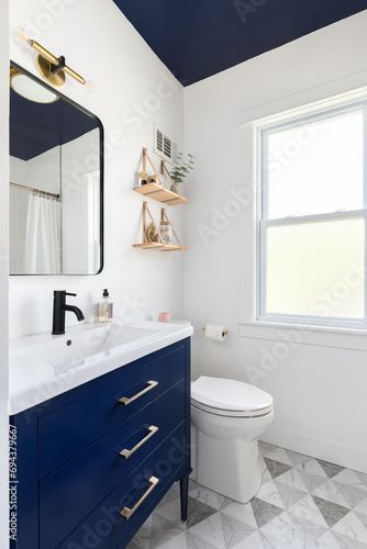 Stock Image: A bathroom with a dark blue cabinet and ceiling, a triangle pattern tile flooring, and decorations decorations on mounted shelves. Bathroom With Blue Ceiling, Navy Blue Accent Bathroom, Triangle Tile Pattern, Dark Blue Bathrooms, Navy Bathroom, Blue Cabinet, Dark Ceiling, Blue Bathroom Vanity, Toilet Room Decor