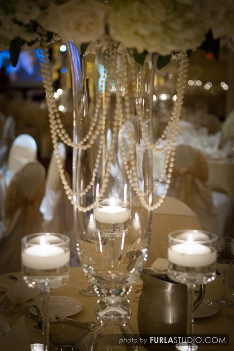 Accents of white hanging pearls add zest to this high table centerpiece. Floating candles in monet candle holders brighten the table. Wedding Party Table Backdrop, Pearl Wedding Decor, Pearl Wedding Theme, Pearl Wedding Decorations, Pearl Theme, Floating Candle Centerpieces Wedding, Floating Candles Wedding, Floral Arrangements Centerpieces, Pearl Centerpiece