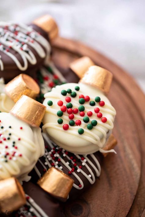 These easy Oreo Christmas Cookies are made with oreos, rolos, almond bark, and sprinkles! Peanut butter stuffed oreos are dipped in white chocolate and topped with a Rolo to look like an edible Christmas ornament! Holiday Oreo Cookie Pops, Oreo Dipped In Chocolate Christmas, Oreo Ornaments Cookies, Holiday Oreo Cookies, Oreo Christmas Ornament Cookies, Christmas Dipped Cookies, Decorating Oreo Cookies, Chocolate Covered Oreos Decorated, Oreo Cookie Decorations