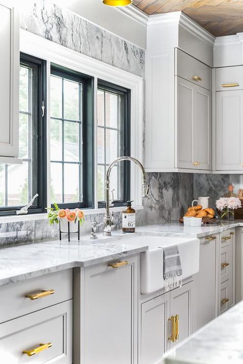 Elegant light gray and gold kitchen is fitted with a farmhouse sink matched with a polished nickel gooseneck faucet mounted to a white and gray marble countertop accenting light gray shaker cabinets adorned with antique brass hardware. Light Grey Shaker Kitchen, Grey Shaker Kitchen, Light Grey Kitchen Cabinets, Light Grey Kitchens, Light Gray Cabinets, Interior Design Career, Gold Kitchen, Grey Kitchen Cabinets, Shaker Kitchen