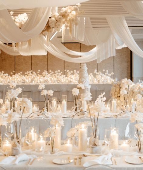 Here’s How To Pull Off a Luxurious All-White Wedding Theme White Cream Ivory Wedding, Off White Wedding Decorations, White Neutral Wedding Decor, Minimal Center Piece Wedding, White And Glass Wedding Decor, Candle Wedding Alter Ceremony Backdrop, Rose Gold White Wedding Decor, Elegant Wedding Styling, White And Candle Wedding