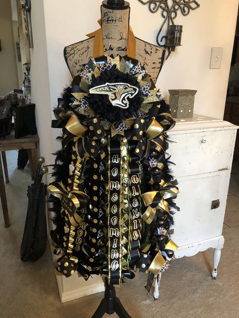 Big and Bold Johnson Jaguars Mega Mum made to a 24 inch ribbon length to accommodate client that was under 5’ tall. Jaguar Homecoming Mum, Mums Homecoming Black And Gold, Black And Gold Mums For Homecoming, Black Homecoming Mum, Black And Gold Homecoming, Hoco Queen, Mums Homecoming Senior, Hoco Mums, Senior Homecoming